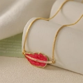 Primo piano della collana dorata con pendente a foglia in smalto rosso e piccoli diamanti - Rosa Acceso