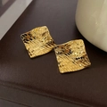 Goldene quadratische Ohrstecker mit gewebter Textur auf braunem Lederhintergrund - Gold (Echt vergoldeter Silberstift) / Gold
