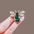 Dettaglio ravvicinato di una spilla a forma di ape con gemma verde e cristalli - Verde