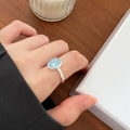 925 sterling silver ring with oval light blue gemstone on finger over wooden desk - Light Blue Oval Gemstone Style(JZ0153)