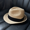 Dettaglio di un cappello di paglia marrone chiaro con nastro nero su pelle nera - Stile con nastro nero