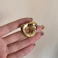 Vista macro de un broche minimalista dorado con forma orgánica sostenido a mano - Dorado