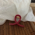 Detail of a curved red hair claw clip with a gold spring on a woven rattan tray - Bright Red