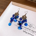 Boho-Ohrringe mit blauen Muschelquasten, Perlen und Metalldetails auf beigem Stoff - Ohrhaken - Königsblau