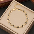 Goldenes Edelstahl-Armband mit Emaille-Augen-Anhängern auf einer beigen Schmuckschatulle - Schwarz