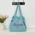 Dettaglio della trama in tessuto waffle azzurro e della scritta Bonjour viola sulla borsa - Azzurro