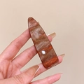 Macro shot of marble textured brown hair clip with water drop shape in hand - Reddish Brown Marble