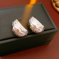 Macro shot of silver C-shaped bean earrings with hammered texture on black jewelry box - Silver