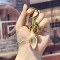 Iridescent conch keychain with golden bell and metal ring shown in hand - Small Yellow Conch