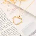 Dettaglio di un ciondolo a cuore dorato con stelle a cinque punte e zirconi su fondo floreale - Stile Heartagram