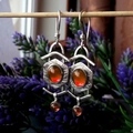 Close-up of vintage silver earrings with orange oval stones against lavender background - Red