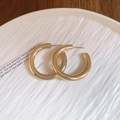 Vista superior de pendientes de aro dorados en forma de C sobre cerámica blanca y madera - Pasador de Acero Dorado - Forma de C Gruesa (Diámetro 3,9 cm)