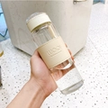 Minimalist glass bottle with beige leather sleeve and lid held against a blurred background - 16oz / With Tea Infuser / Beige