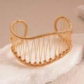 Dettaglio del bracciale a polsino intrecciato dorato con perline su una pietra bianca - Oro
