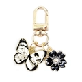 Close-up of golden keychain with black and white enamel butterfly skull and flower charms - Profile Skull Butterfly + Black Cherry Blossom