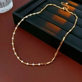 Dettaglio di collana dorata con perle e tubi metallici su superficie in pelle rossa - Oro-Bianco