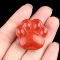 Hand holding a red jasper gemstone carved in a cute animal paw print shape - Red Jasper