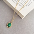 Gros plan du collier étoile dorée avec pierre de malachite verte sur un livre vintage - Collier en Acier Titane Texture Malachite Ovale Vert