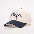 Detailed embroidery of Doing My Best text and blue bow on contrast baseball cap - Cream/Navy Blue