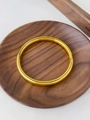 Bracciale rigido in acciaio al titanio placcato oro su un vassoio rotondo in legno - Oro Lucido