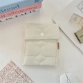 Close-up of quilted cream sanitary napkin storage pouch with button and red woven label - White