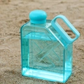 Clear square plastic fitness water bottle with blue handle and cap on beach sand - Blue
