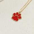 Golden necklace with red enamel cat paw pendant on a textured beige background - Red