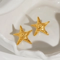 Close-up of gold starfish earrings with spiral texture on white ceramic plate - Earrings (Pair)