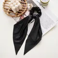 Detail of black pleated satin scrunchie with long ribbons on an aesthetic magazine layout - Glossy Black Streamer