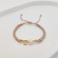 Detailed shot of handmade woven bracelet with freshwater pearl and golden letter E charm - Letter E