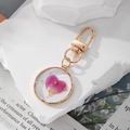 Round resin keychain featuring a pink heart-shaped dried flower petal and gold foil - Rose Red Petals