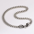 Detailed close-up of punk style skull heads and chunky silver metal Cuban link chain - 13mm / Steel