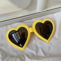 Detail shot of yellow heart-shaped sunglasses with dark lenses on white fabric - Small Heart Yellow