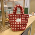 Detail der rot-weiß karierten Lammwoll-Tasche mit gewebtem Markenetikett auf einer Theke - Rot Karo
