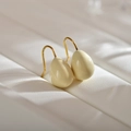 Close-up of cream teardrop earrings with gold hooks on a white leather texture background - White