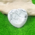 White marble heart worry stone with grey veins displayed on natural green grass - Howlite