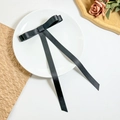 Détail d'une pince à cheveux avec nœud en satin noir posée sur une assiette décorative - Noir
