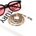 Detail of bohemian colorful woven eyewear lanyard with metal clips on a white book - US 15