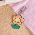 Acrylic flower keychain with orange petals and smiley face on a cork background - Little Flower