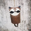 Detail view of a rustic raccoon wind chime hanging by a rope against a stone wall - Red Panda