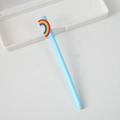 Light blue cartoon gel pen with a 3D rainbow topper on a clean white desk surface - Rainbow