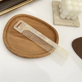 Detail eines cremefarbenen Marmor-Acetat-Kamms mit breiten Zinken auf einem Holztablett - Weiß