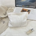 Detail of white lace makeup bag with heart bow embroidery on textured fabric background - White