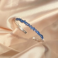 Brazalete abierto plateado con circonitas azul oscuro rectangulares sobre fondo de seda champán - Circonita Azul Chapado en Oro Blanco