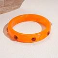 Detailed macro view of orange acrylic resin bangle with red gemstone accents and gold claws - Orange