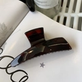 Detailed view of large dark amber tortoiseshell hair claw clip on a white book - Glossy Red Brown