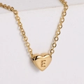 Close-up of 18k gold plated heart necklace with engraved letter E on textured background - Letter E
