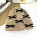 Detail shot of beige knit hat with velvet bows on a minimalist tabletop setting - Khaki