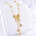 Dettaglio di una collana dorata con ciondolo a fiocco e tre nappine di zirconi a goccia - Collana