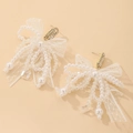 Detalle de pendientes de lazo con encaje, perlas y cristales sobre un fondo melocotón - Pin de Plata - Pendientes de Lazo Blanco